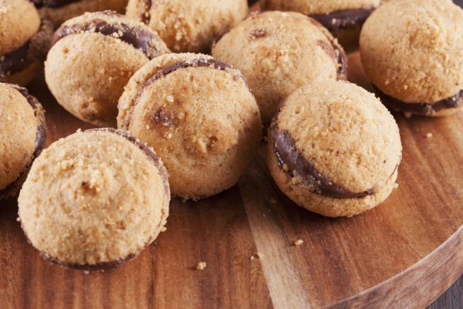 Baci di dama con farcitura al cioccolato fondente: una ricetta tipica del Piemonte Tagliere di legno con biscottini di baci di dama al cioccolato