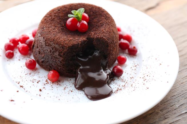 Torta al cioccolato con cuore morbido, un dolce golosissimo dal ripieno cremoso e fondente Torta al cioccolato su piatto da portata bianco con decorazione di ribes rossi