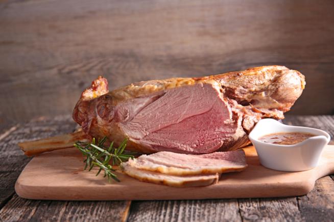 Agnello al forno: la ricetta Agnello cotto al forno con rosmarino su tavolo da cucina bianco.