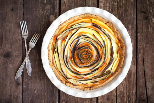 Torta vegetariana di verdure a spirale con zucchine, carote e melanzane Torta salata con verdure disposte a spirale su tavolo di legno grezzo