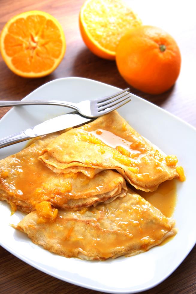 Come preparare delle crêpe suzette: ricetta facile e veloce Crêpes con salsa di arancia su piatto quadrato con arance tagliate a metà