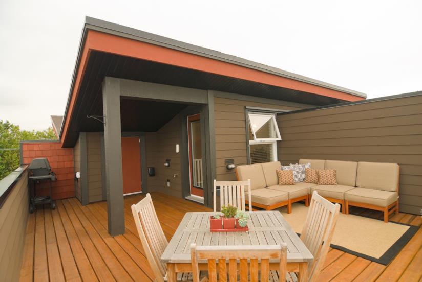 Idee per arredare la terrazza durante la stagione calda Terrazza con pavimento in legno, sedie e tavolo, due sofà e un piccolo barbeque nell'angolo