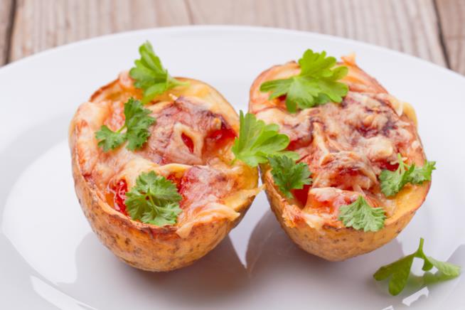 Patate farcite: la ricetta Primo piano di due metà di una patata con all'interno pomodoro, mozzarella e prezzemolo su piatto