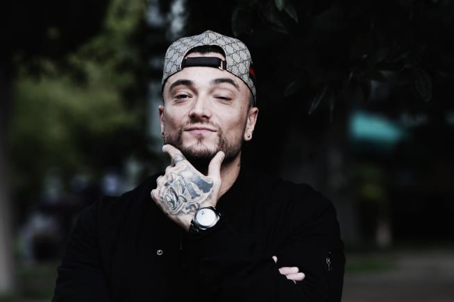 Borsello è il nuovo singolo di Gué Pequeno con Sfera Ebbasta Primo piano di Gué Pequeno, con la mano sul mento, una felpa nera e il cappellino al contrario