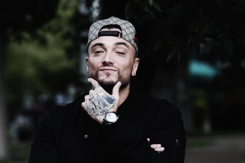 Borsello è il nuovo singolo di Gué Pequeno con Sfera Ebbasta Primo piano di Gué Pequeno, con la mano sul mento, una felpa nera e il cappellino al contrario