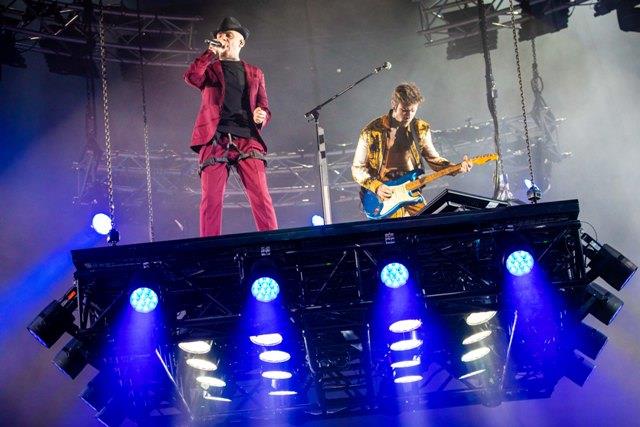 Fedez e J-Ax a San Siro J-Ax in rosso, Fedez con la giacca aperta, che suona la chitarra, entrambi su un palco sollevato da terra