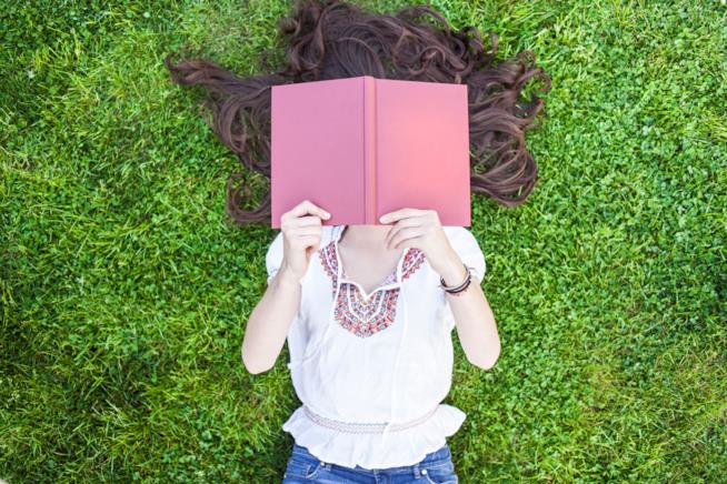 L'importanza della lettura per i ragazzi di nuova generazione Ragazza che legge sdraiata in un prato