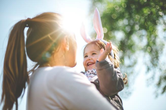 Poesie per la Pasqua Una donna tiene in braccio una bambina con orecchie da coniglio