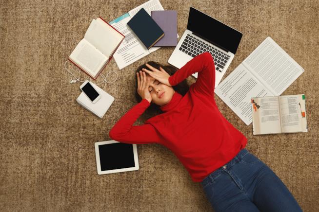 Una ragazza sdariata a terra tra libri e computer Una ragazza con la testa tra le mani