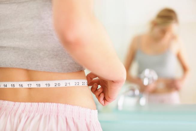 La dieta emozionale per dimagrire senza stress e attacchi di fame Una ragazza allo specchio si misura con il centimetro