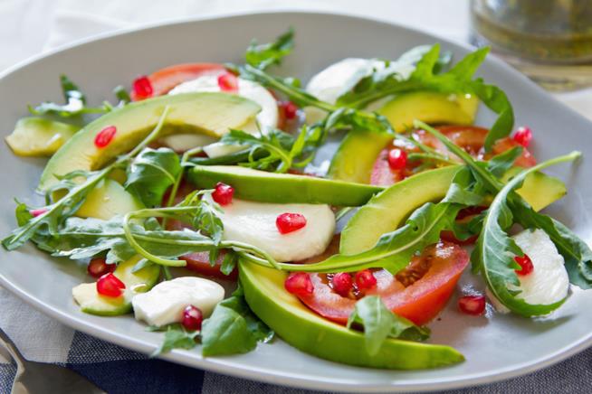 Caprese esotica: la ricetta Primo piano su piatto bianco di avocado, mozzarella, rucola e melograno