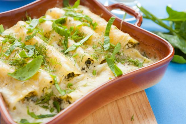 Cannelloni ripieni: la ricetta Tegame in terracotta in primo piano con cannelloni ripieni di ricotta e spinaci, su base di legno