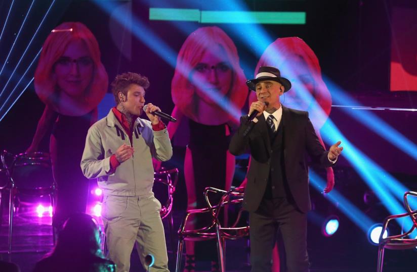 Fedez e J-Ax ospiteranno anche Cris Brave Fedez in grigio, J-Ax in nero cantano in piedi al microfono con lo sfondo del volto della Ferragni