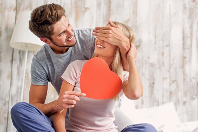 Le frasi di San Valentino da dedicare a lei Un ragazzo abbraccia una ragazza facendole la sorpresa di un cuore di cartone