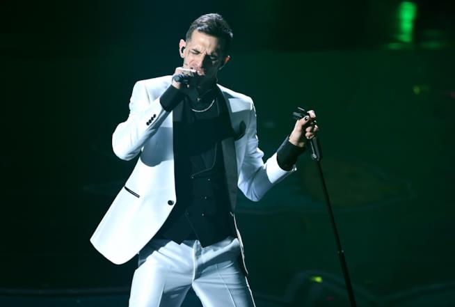 Achille Lauro Achille Lauro, vestito di bianco, canta in piedi con in mano il microfono