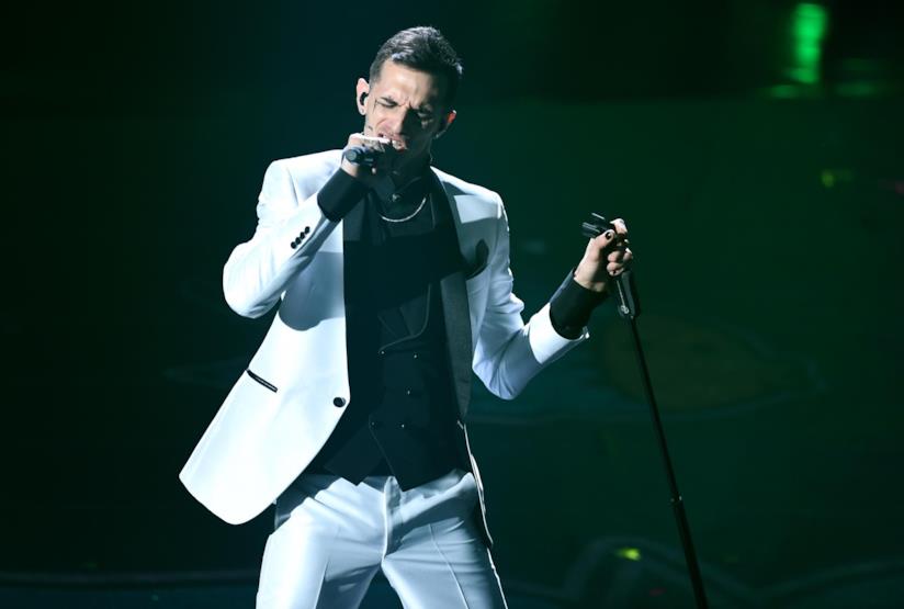 Achille Lauro Achille Lauro, vestito di bianco, canta in piedi con in mano il microfono