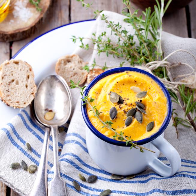 Vellutata di zucca con semi di girasole: la ricetta Tazza bianca con bordo blu con all'interno vellutata di zucca, semi di girasole e crostini di pane