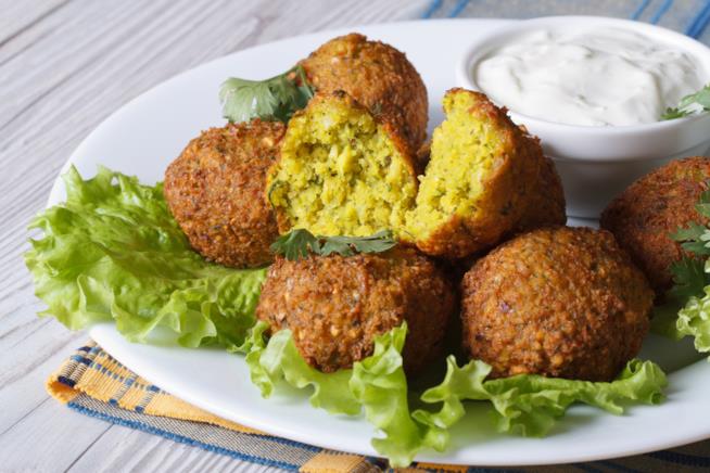 Falafel: la ricetta Primo piano di falafel di ceci su piatto bianco, con foglie di lattuga e salsa allo yogurt