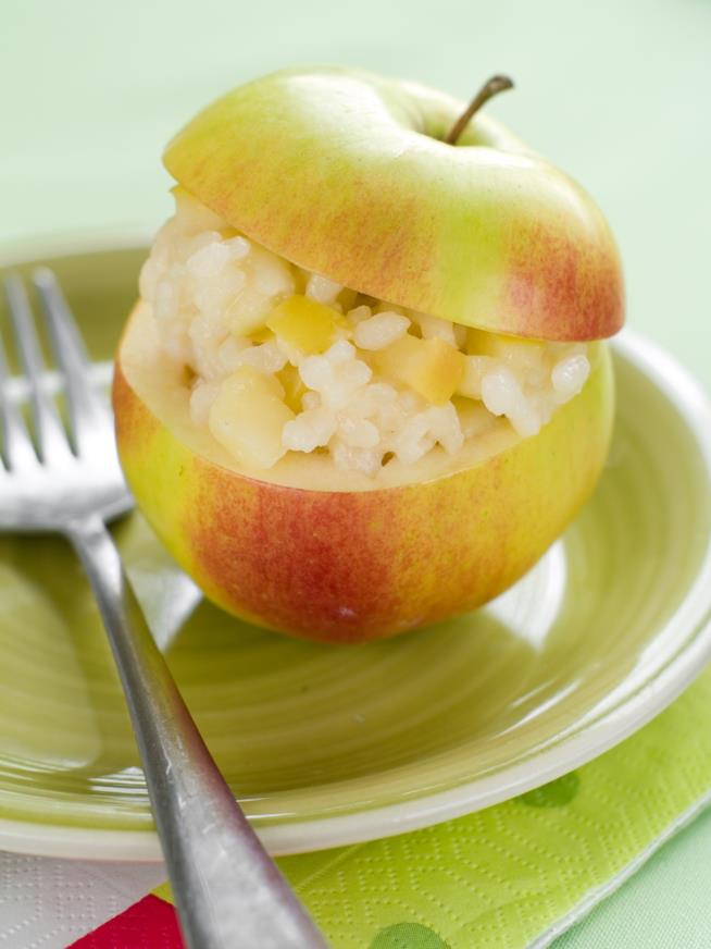 Risotto di mele: la ricetta Primo piano di un piatto verde con forchetta, una mela scavata e all'interno riso con le mele