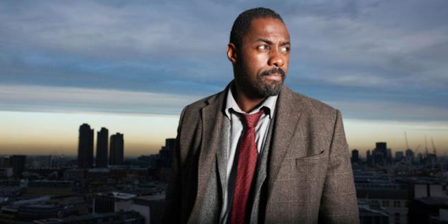 Il detective John Luther sta per tornare! Mezzobusto di Idris Elba con città sullo sfondo, all'alba