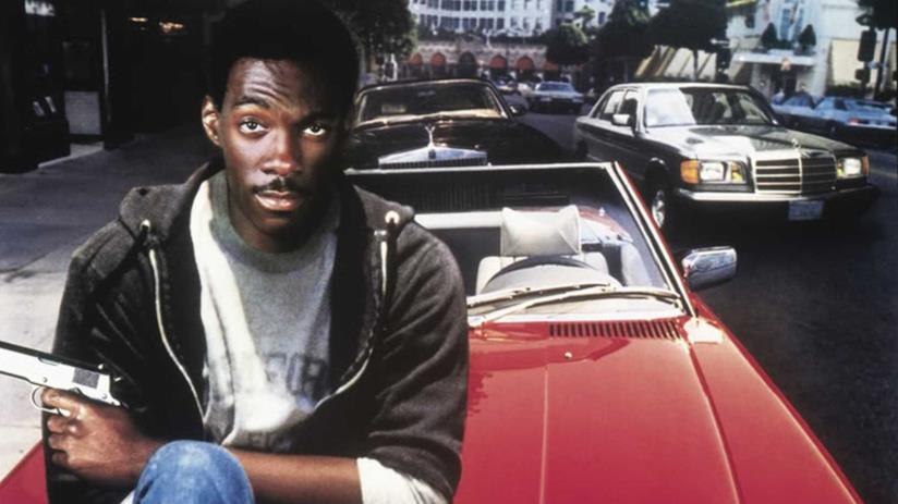 Eddie Murphy vuole continuare la saga di Beverly Hills Cop con un quarto capitolo Eddie Murphy nei panni di Axel Foley con una pistola in mano seduto sul cofano di una auto rossa
