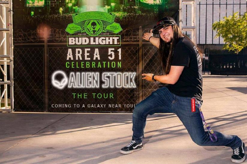 Area 51: gli ultimi preparativi, tra nuovi MEME e le prove per correre come Naruto Matty Roberts con dietro il cartellone ufficiale del festival Alienstock