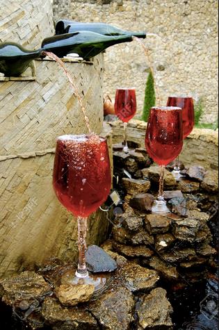Una fontana di vino rosso con i bicchieri pronto Una fontana eroga vino rosso sulle rocce