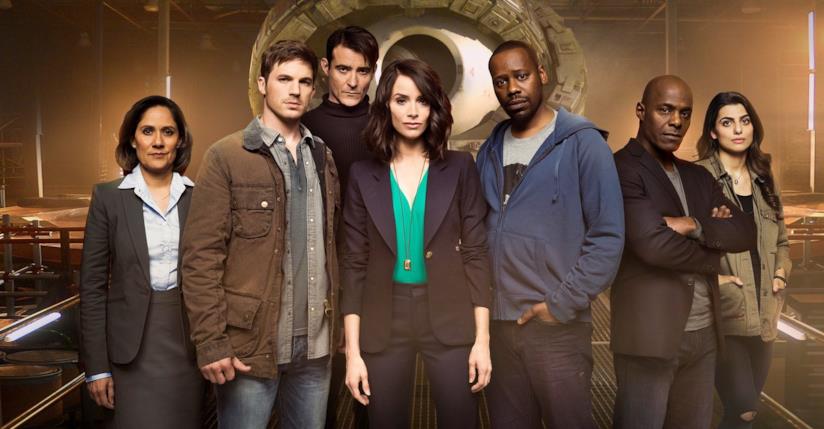 Il cast di Timeless I protagonisti del telefilm, in piedi, e la macchina per viaggiare nel tempo sullo sfondo